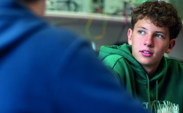 Enthusiastic teenage boy in green hoodie participating in summer boarding course activities at an educational camp.