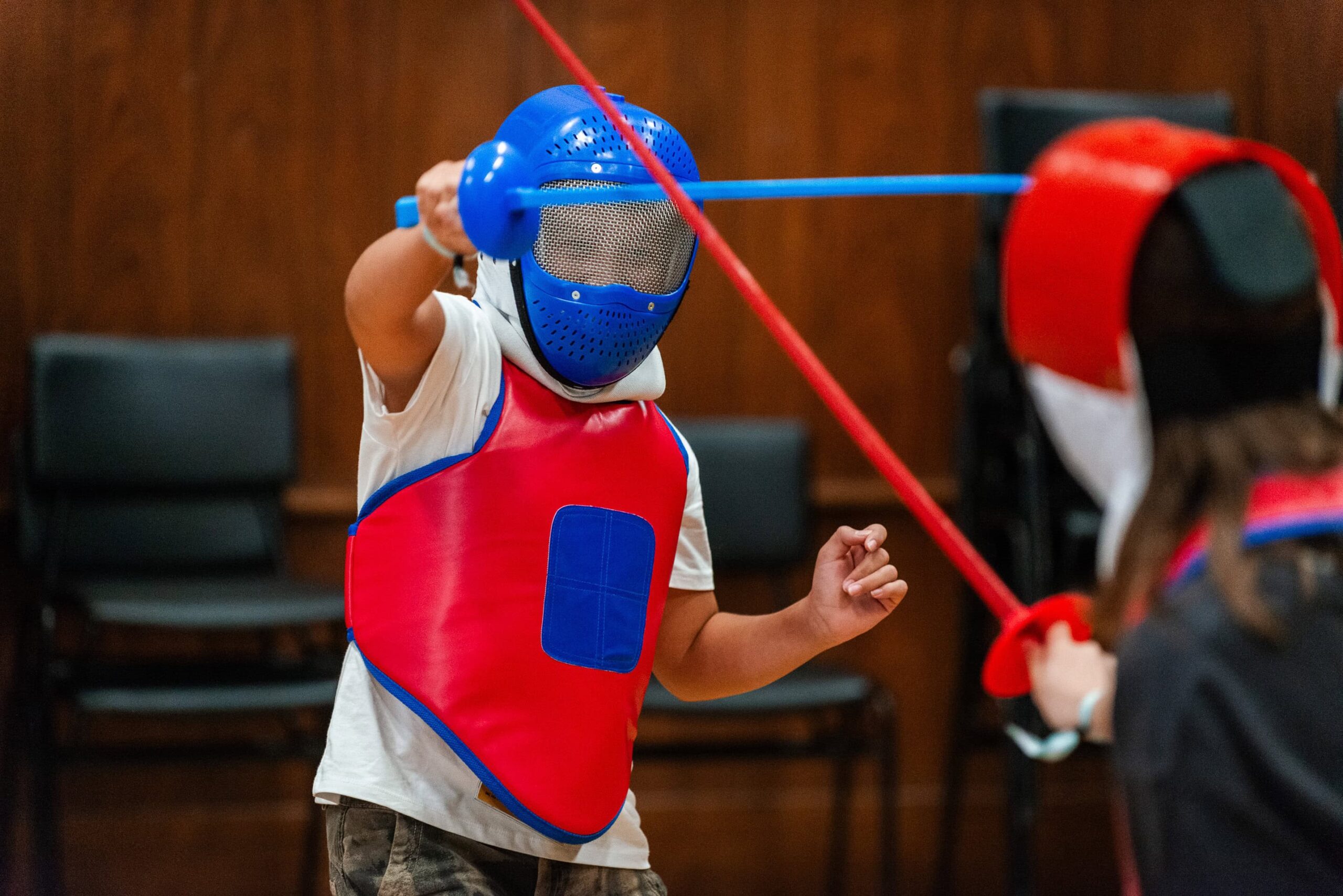 Bright blue fencing mask and red protective gear worn by children during fencing class at summer boarding course